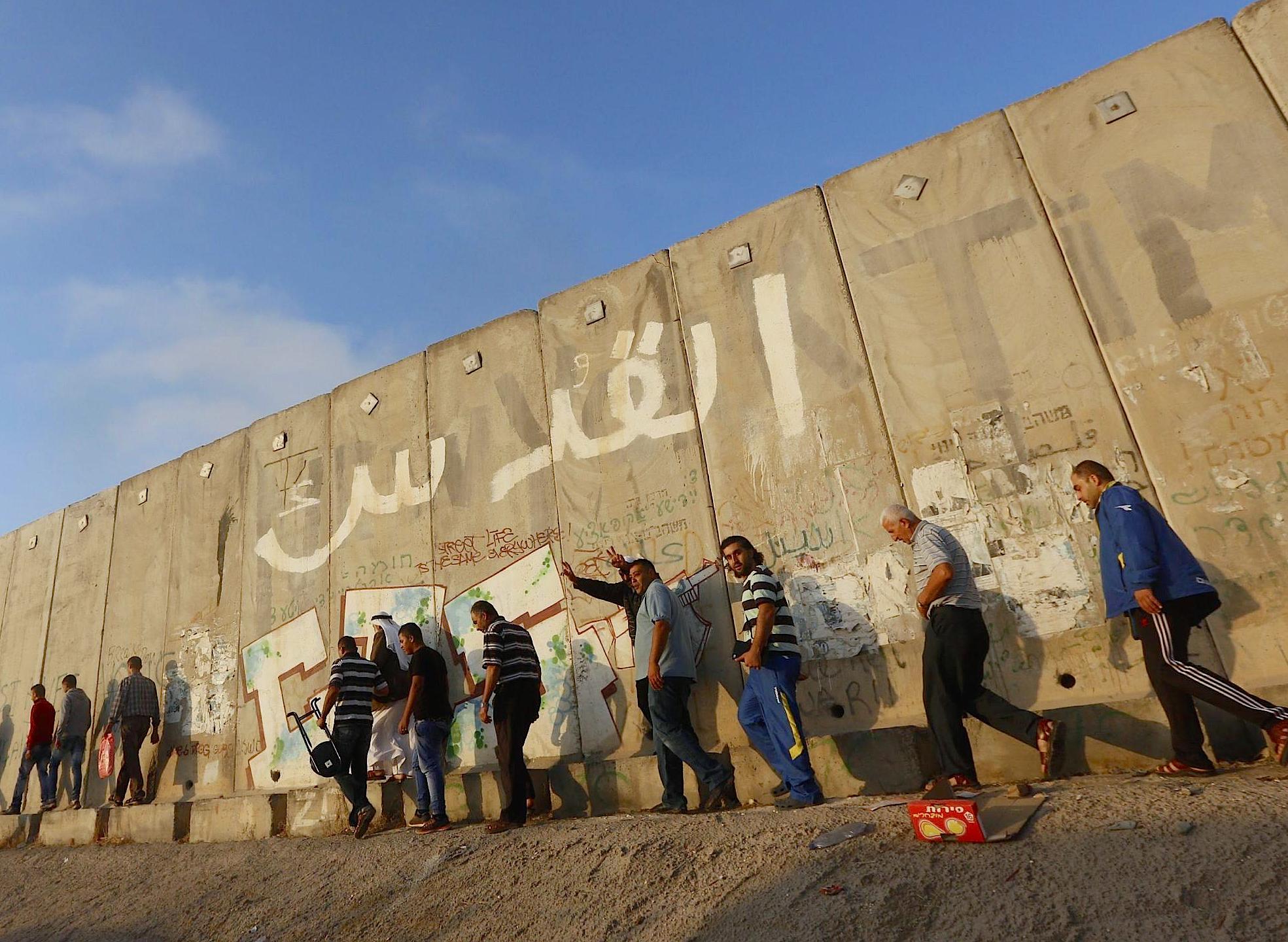 Palestinian men walk next to the Israeli West Bank seperation barrier - wall