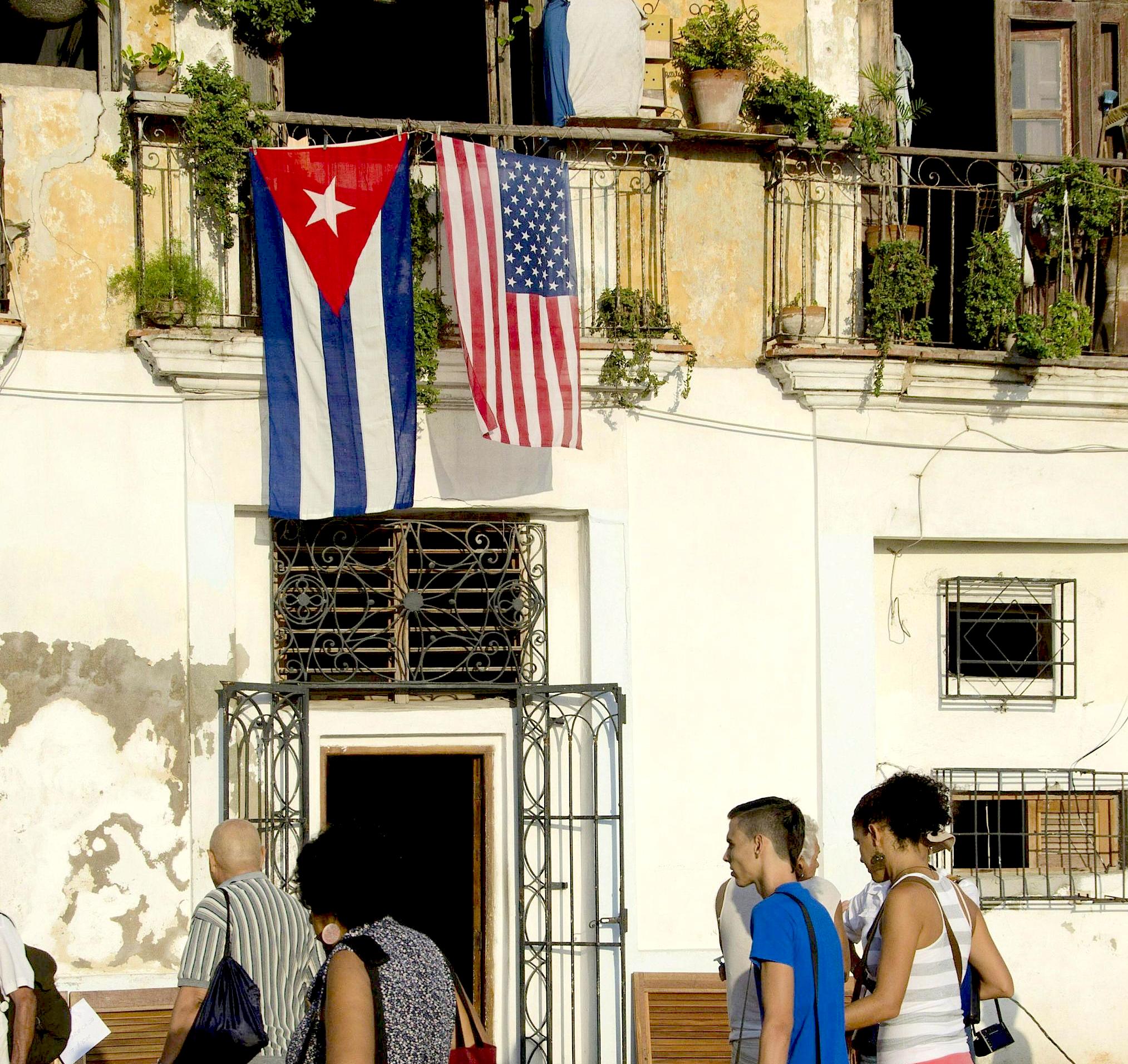 People walk by a balcony with the flags of USA and Cuba in Havana