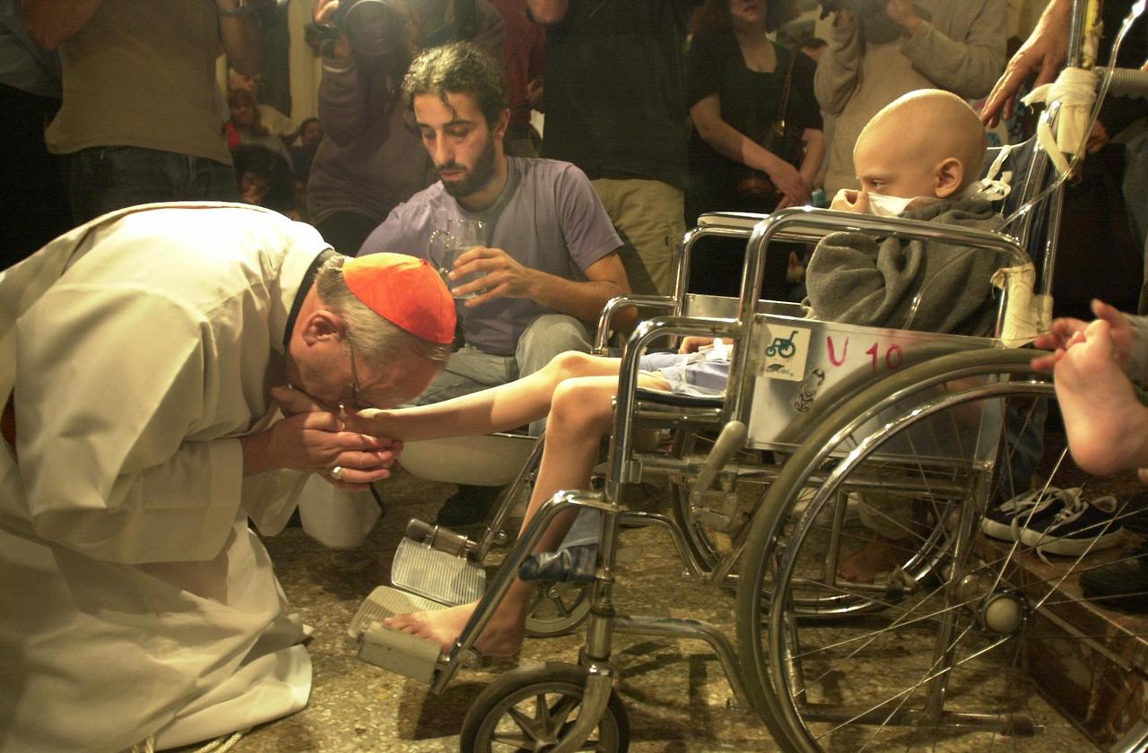 Cardenal Bergoglio besa los pies de un niño enfermo. Foto de archivo
