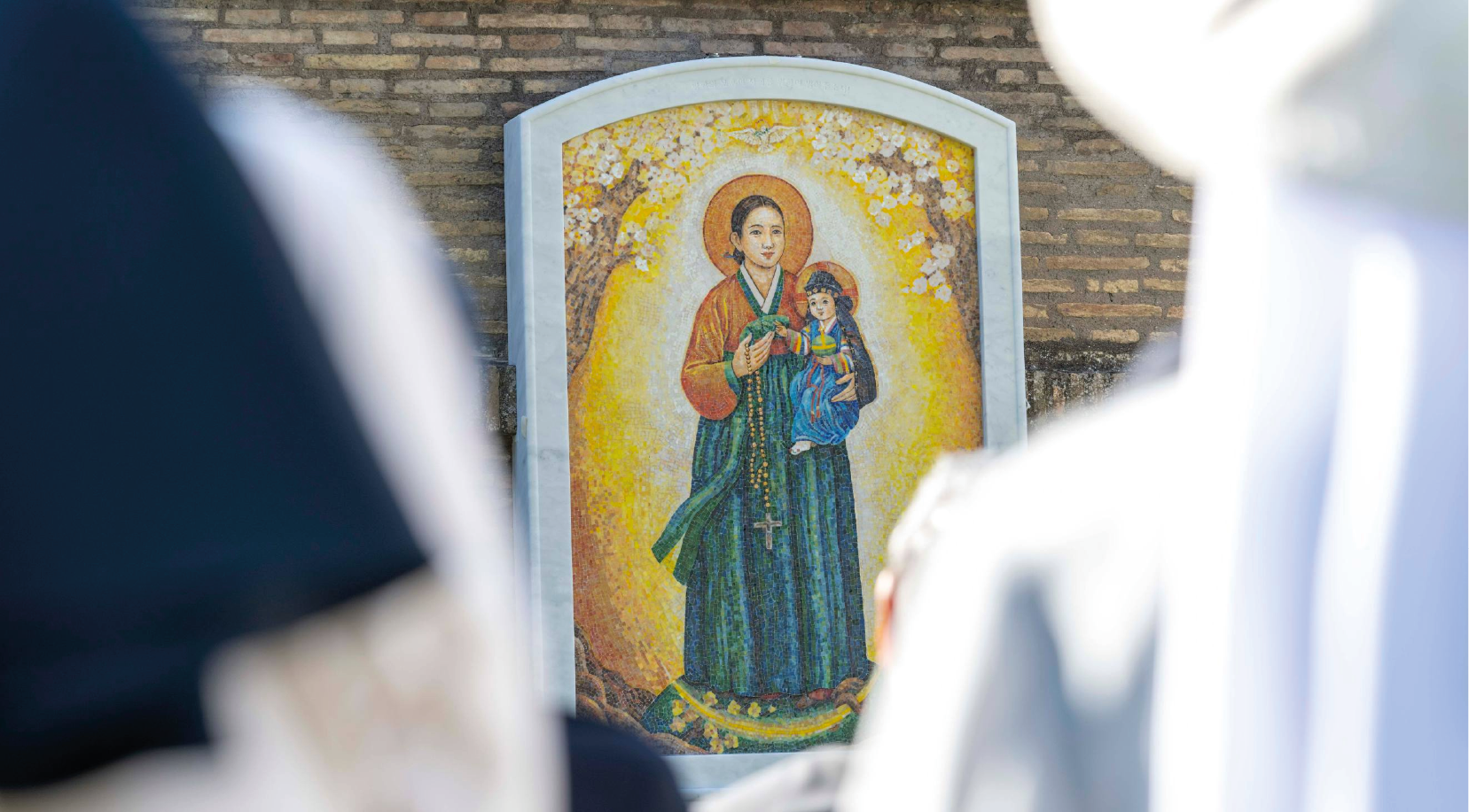 La Virgen María, vestida con un “hanbok” coreano tradicional, se erige como una figura de cuidado maternal y protección divina.